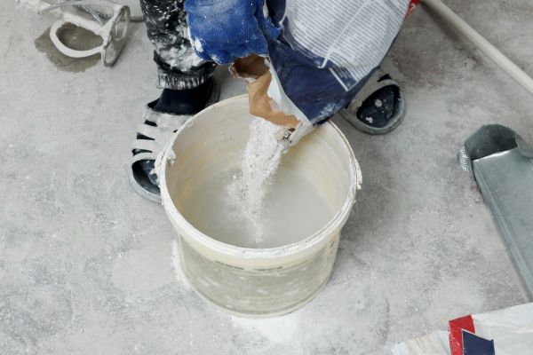 Angle view of plaster powder being poured into a bucket of water.