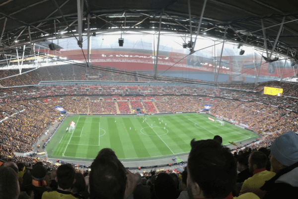 Interior view of Wembley Stadium, showcasing the vibrant atmosphere during a football match, with fans in the stands and the iconic arch in the background.