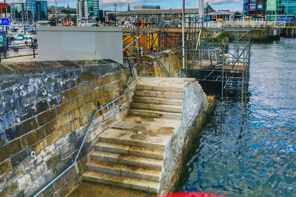 The Mayflower Steps in Plymouth, England, leading down to the waterfront, with historical plaques and the Mayflower Memorial nearby.