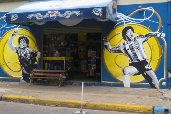 Murals of Diego Maradona on both sides of a shop entrance in La Boca, Buenos Aires, celebrating his legendary status in Argentine football."