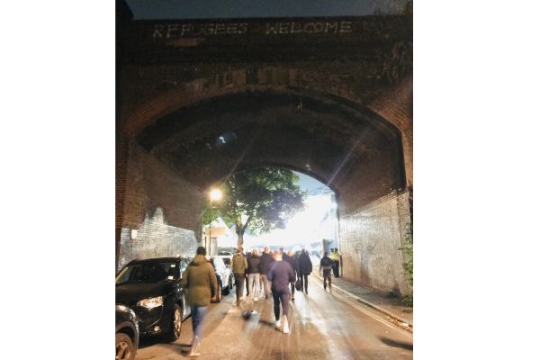 Fans walking under a railway arch towards Millwall Stadium on matchday, creating an energetic atmosphere.