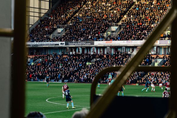 Football match in action at Turf Moor Stadium with players on the pitch and fans in the stands.