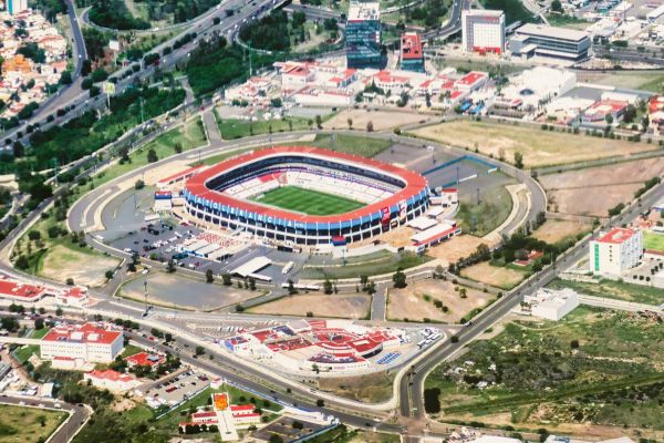 Aerial view of Estadio Corregidora in Querétaro, Mexico, showcasing its oval structure surrounded by lush greenery and cityscape.