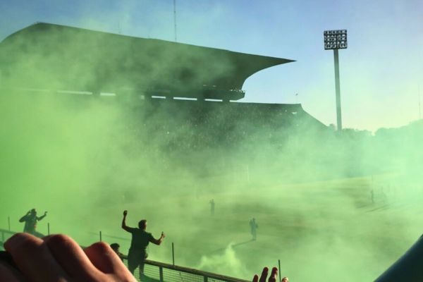 Ferro Carril Oeste fans cheering behind the goal, surrounded by green smoke before a match at Ferro Stadium.