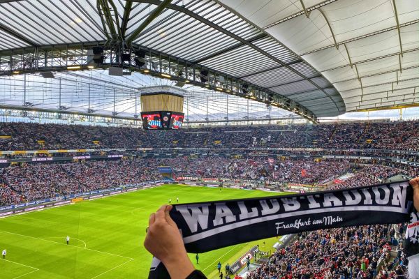 A fan holding a Waldstadion scarf in the stands of Eintracht Frankfurt’s stadium during a matchday, surrounded by a vibrant crowd.