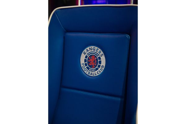 Close-up of the Rangers badge on the back of a dugout seat at Ibrox Stadium.