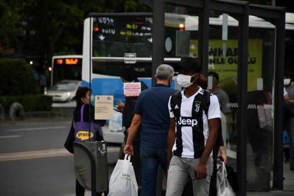 A man walking along a city street wearing a black-and-white striped Juventus football shirt, surrounded by urban buildings and a casual atmosphere.