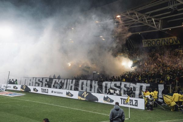 Passionate FC Nantes fans in the stands with colorful smoke from flares during a match at Stade de la Beaujoire.