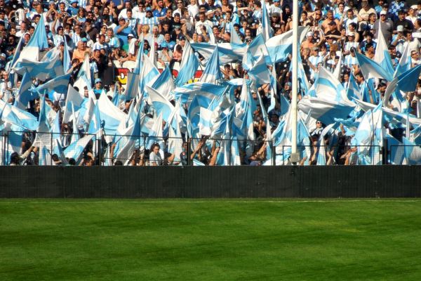 Racing Club fans waving flags in club colors pitchside at Estadio Presidente Perón.