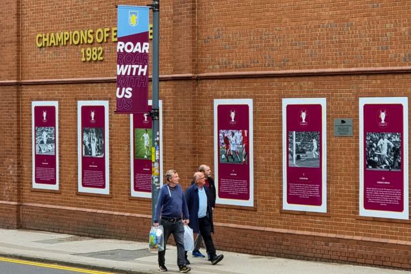 Group of people walking outside the brick wall of Villa Park Stadium.