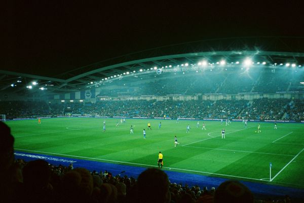 Match night at Brighton’s Amex Stadium, with the pitch illuminated under the floodlights and fans creating an electric atmosphere in the stands. The stadium is home to Brighton & Hove Albion FC.