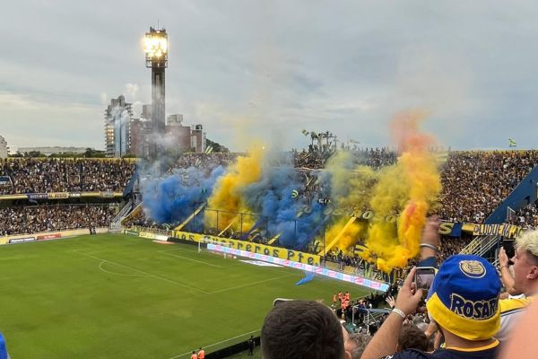 Blue and yellow smoke filling the air above one end of Estadio Gigante de Arroyito on matchday, creating an electrifying atmosphere at a Rosario Central game.