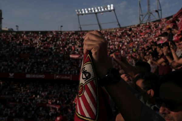 A passionate Sevilla FC fan holding a scarf in the Ramón Sánchez-Pizjuán Stadium on matchday, surrounded by cheering supporters.