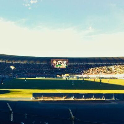 A soccer match featuring Real Potosí at Estadio Ramón Tahuichi Aguilera, one of the highest stadiums in the world, with players in action on the green field under a clear sky.